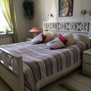 Dubbelsäng med vit sängram och lampor på vit byrå bredvid sängen. 