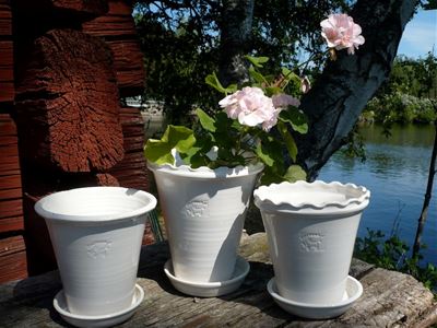 Three white glazed ceramic pots, in one of them a white pelagon, water in the background.