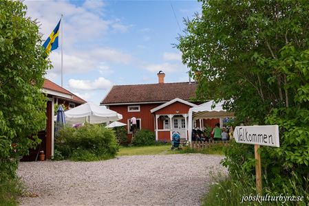 Gårdsbild med rött hus, flaggstång med svenska flaggan.