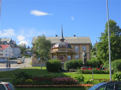 Historic building with a dome and front garden, statue and flower beds in the foreground.