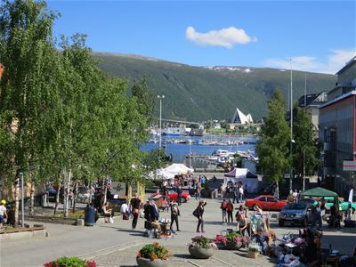 Lively town square with stalls, benches, and a view of the harbour and mountains in the background.