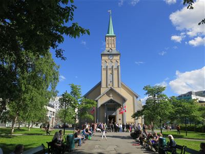 The cathedral with Norwegian flags, surrounded by people and trees on a sunny day.