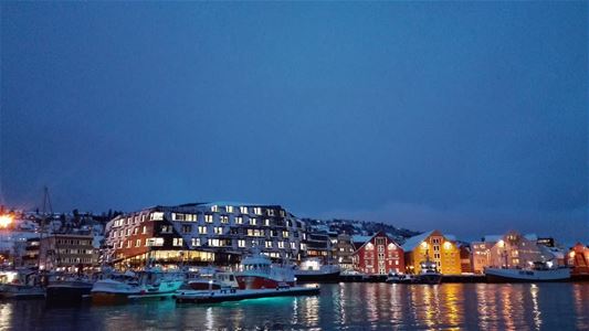 Evening harbour scene with boats and illuminated buildings.
