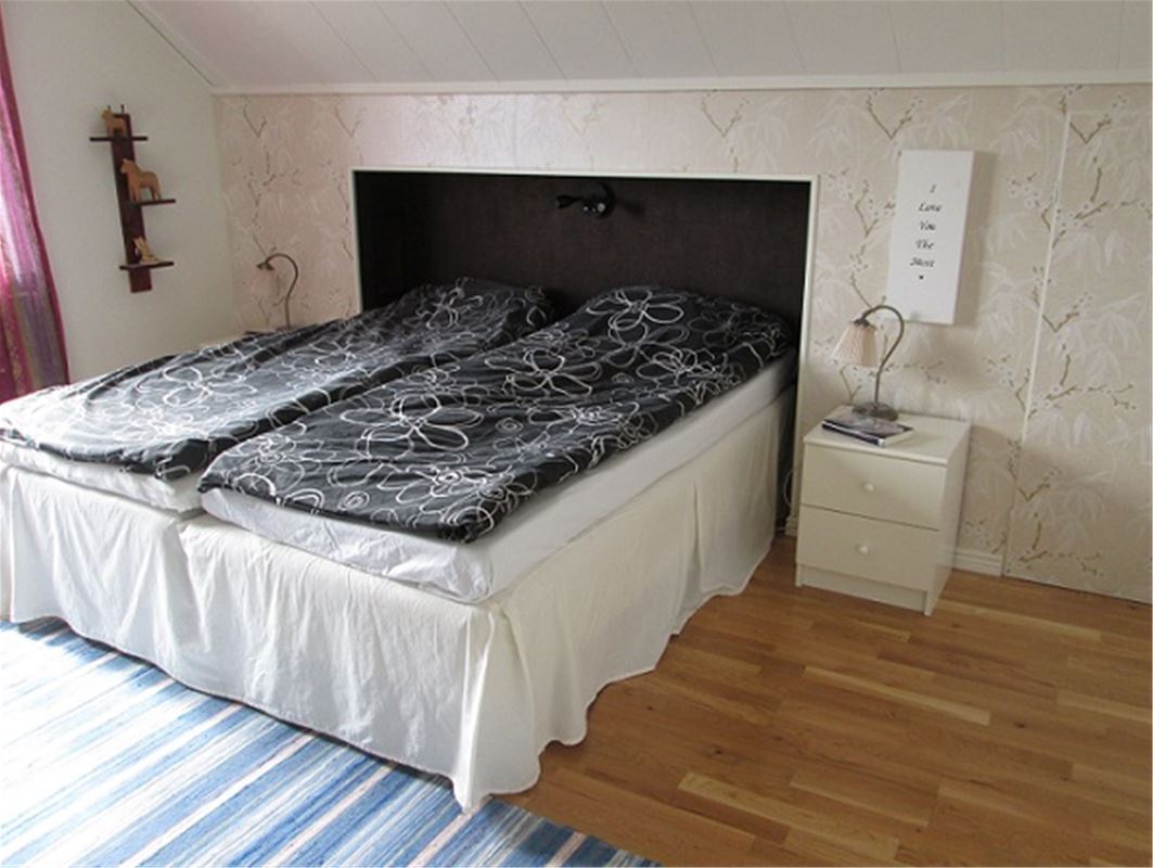 Dubbelsäng med svart sänggavel och vit sängkappa bäddat med svarta påslakan med vita blommor. 
