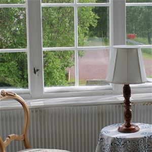 Detail from paned windows with antique chair and small table with a lamp.