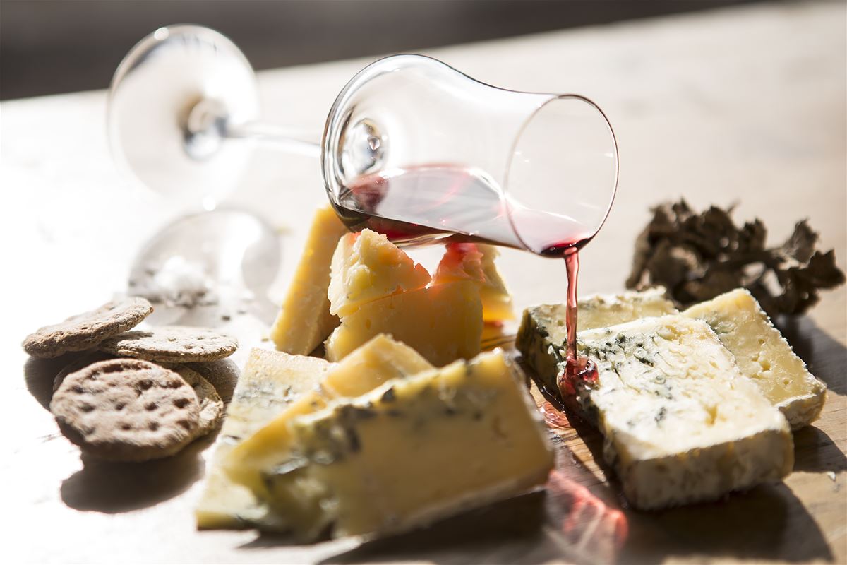 Olika ostar upplagt på ett fat med kex och ett glas vin.