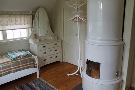 White tiled stove, white wooden sofa and a white bureau with a mirror. 