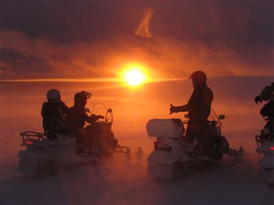 Two snowmobiles crews stand still and watch the sunrise.