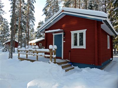 Rödmålad timmerstuga i snö.