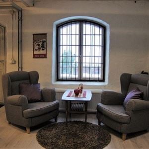 Two grey armchairs and a small table between in front of a barred window.