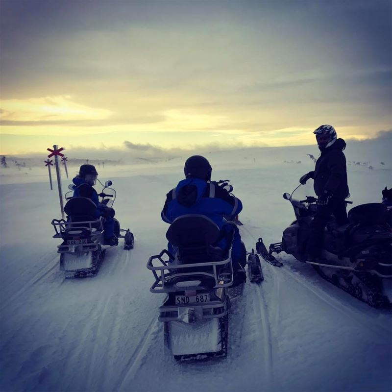 Snowmobile riders on a snowmobile trail in a mountain environment.