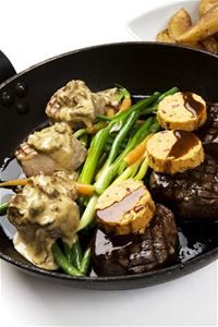 Svart stekpanna med köttbitar svampsås grönsaker och kryddsmör.