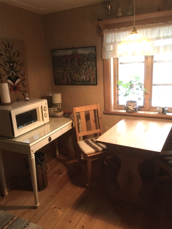 Table by the window with a chair and another table with microwave on standing beside the chair. 