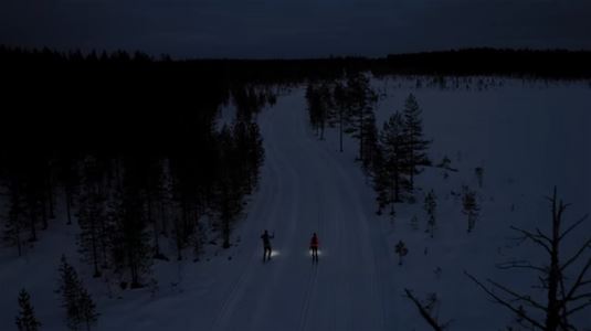 två skidåkare med pannlampor åker i spåret i mörker