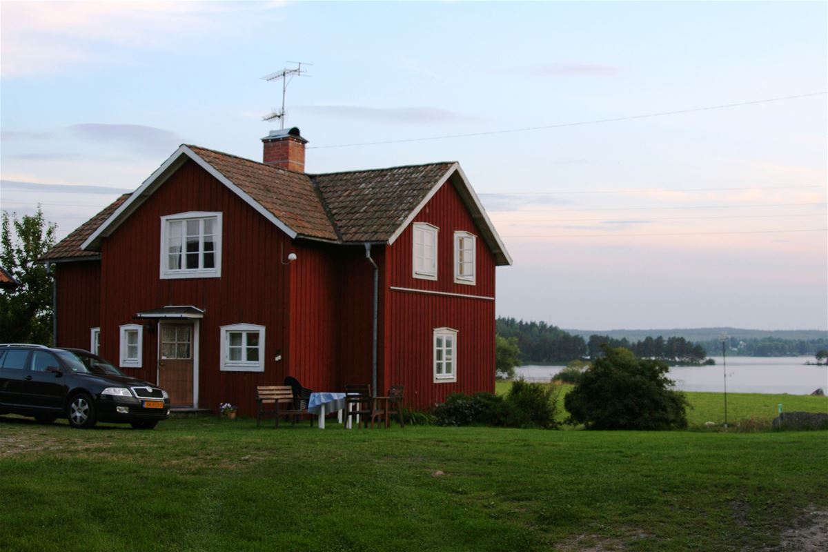 Rödmålat hus på gård med närhet till sjö.