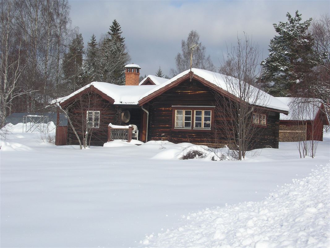 Brown timber cottage with snow-covered roof and lawn. 