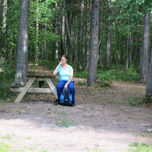 A woman is resting on a bench table in the woods.