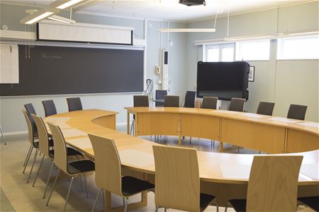 Konferenslokal med stort u-format bord med stolar riktat mot en svart griffeltavla.