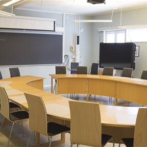 Konferenslokal med stort u-format bord med stolar riktat mot en svart griffeltavla.