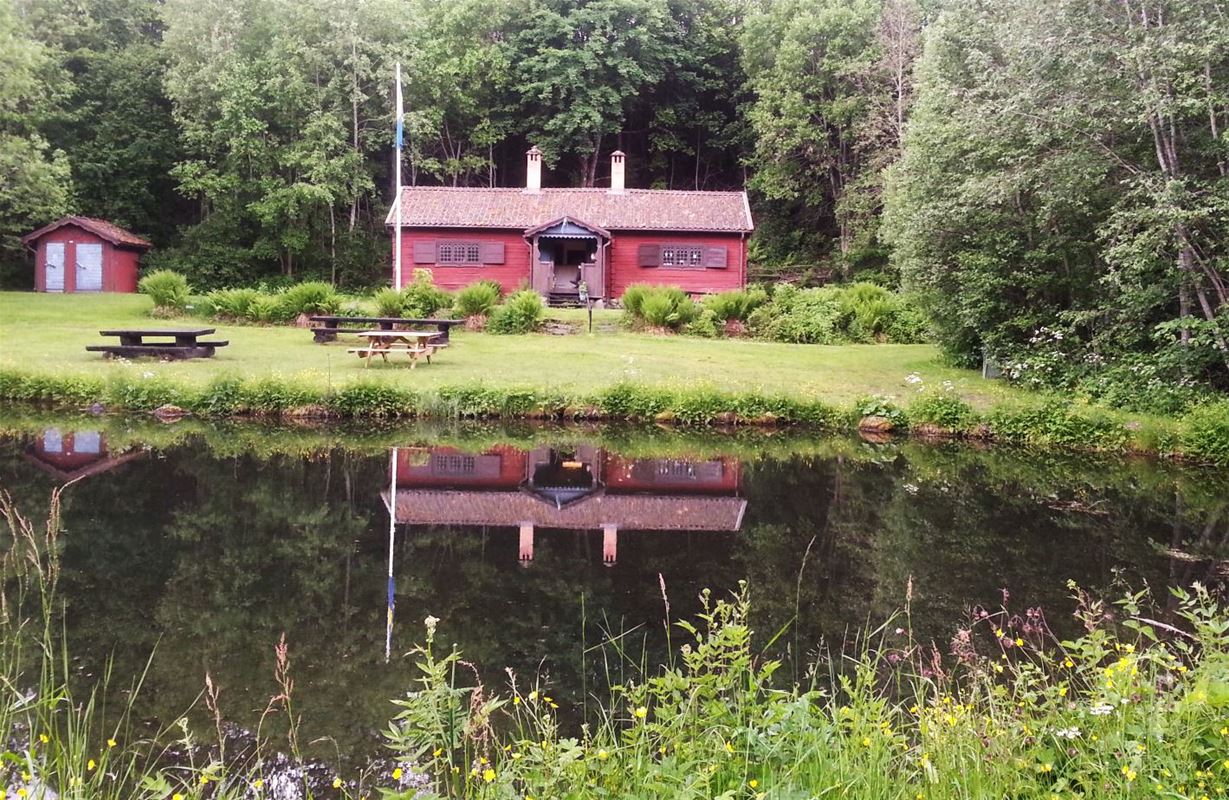 Exterior of red cottage as reflected in the water.