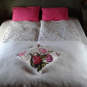 Bed with white and floral bedlinen and floral and red pillows.