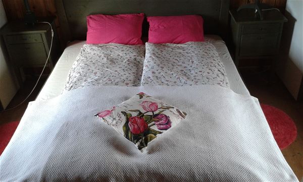 Bed with white and floral bedlinen and floral and red pillows. 