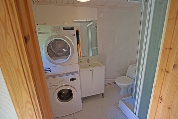 Badrum med tvättmaskin, torktumlare, duschkabin, toalett och handfat. 