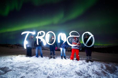 People under the Northern Lights with 'TROMSØ' written in light in the air.