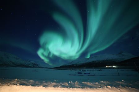 Northern Lights over a snowy landscape with mountains in the background.