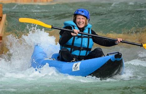 Kvinna i blå hjälm och blå flytväst paddlar i strömt vatten.
