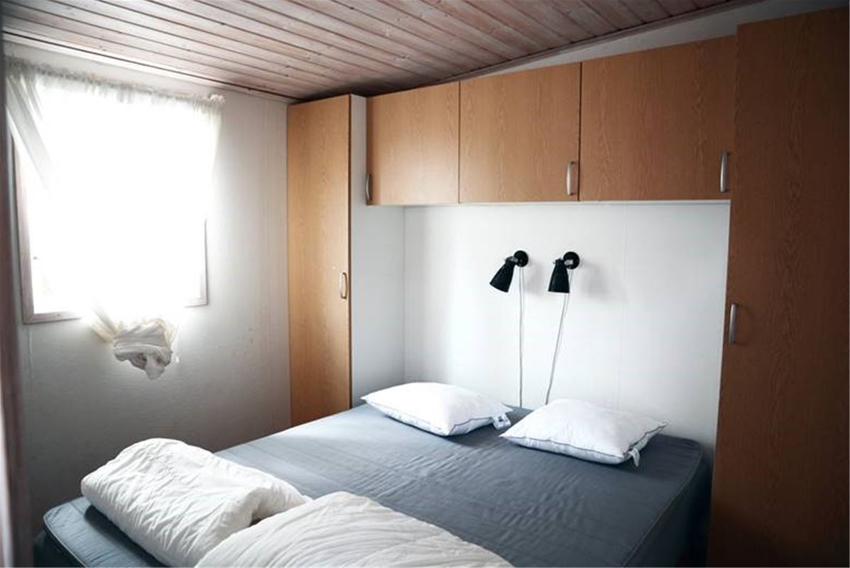 Interiörbild på sovrum, dubbelsäng, sänglampor, skåp ovanför sängarna, garderober brevid sängarna.