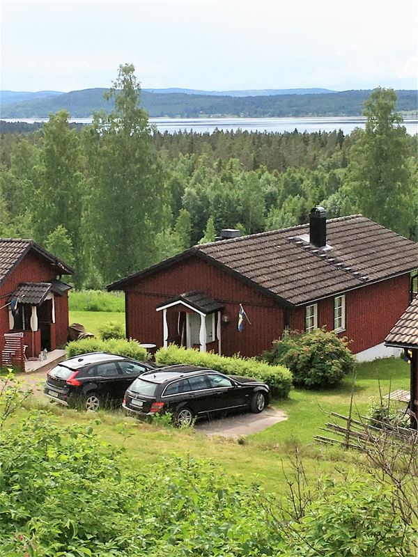 Two cars parked in front of a red cabin with black roof. 