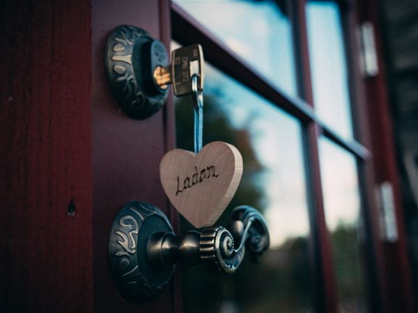 Detalj på dörrhandtag med nyckel i dörren och ett hjärta av trä som nyckelring. 