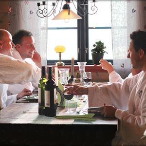 Fyra personer i vita badrockar sitter vid ett bord och dricker vin. 