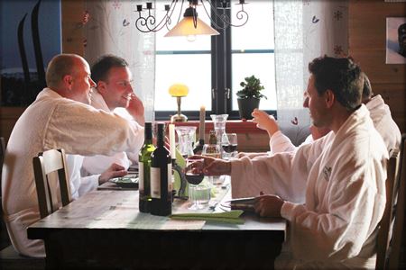 Fyra personer i vita badrockar sitter vid ett bord och dricker vin. 