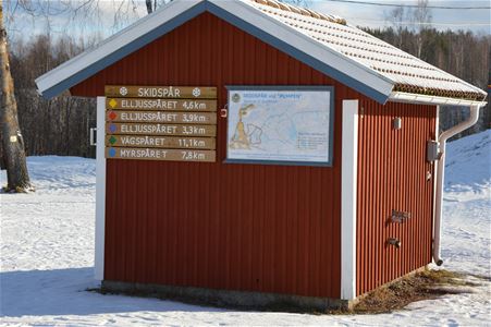 Röd liten byggnad med karta över spåren samt skyltar med spårens namn och längd.