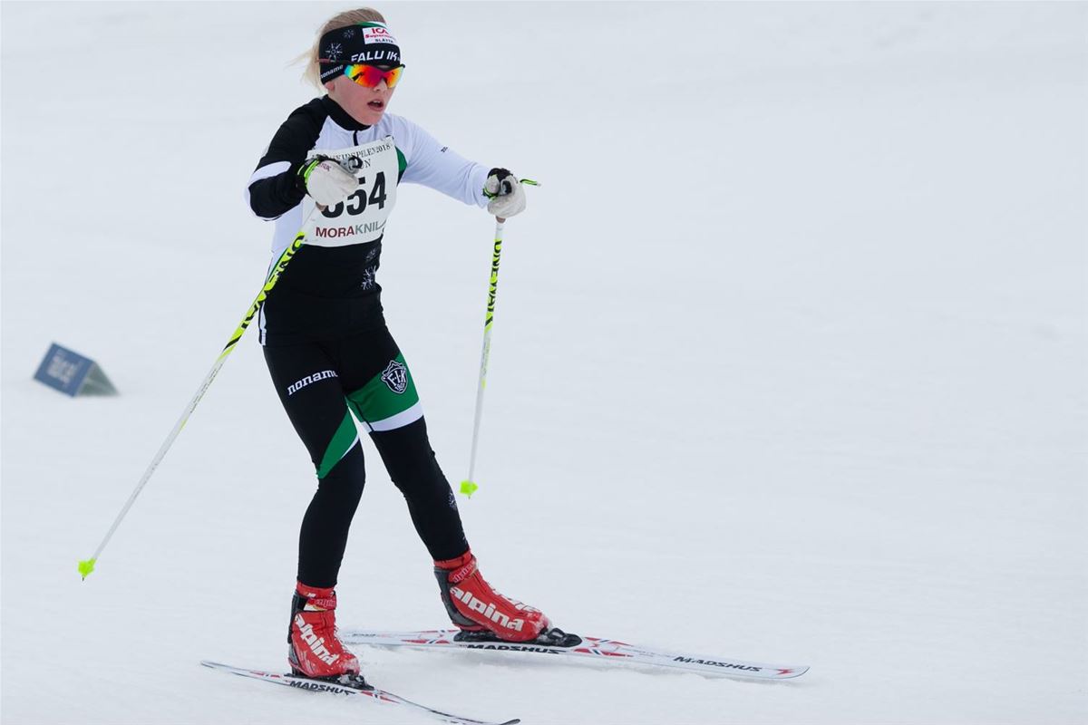 En tjej i svart, vit och grön klubbdräkt som åker längdskidor.