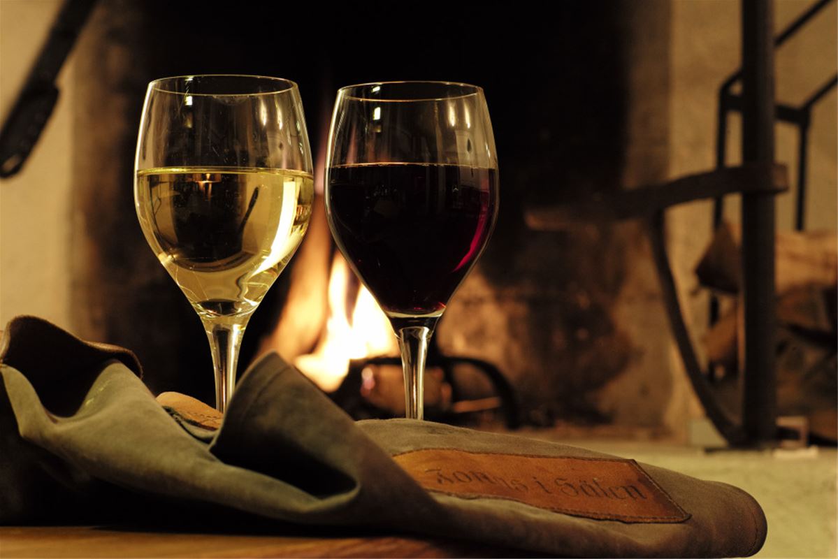 Two filled wine glasses and a fire in the background.