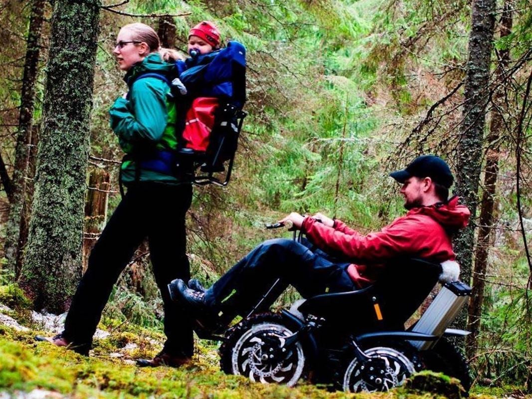 Man i rullstol och kvinna som bär ett barn på ryggen.