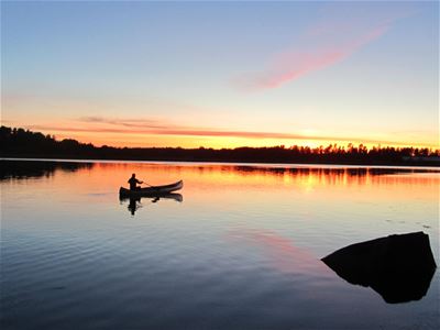 Kanot mitt på sjön i solnedgång.