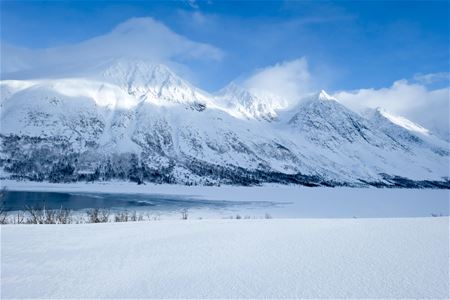 Snødekte fjell bak frossen innsjø