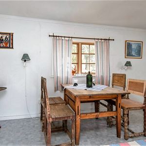 Vitmålat rum med antikt matbord och stolar vid ett fönster. 