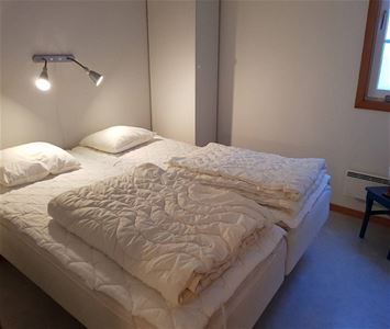 Dubbelsäng i ett vitt rum med en sänglampa ovanför på väggen. 