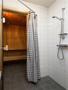 Öppen bastudörr och en kaklad dusch med prickigt duschdraperi. 