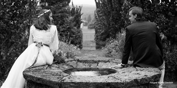 Black and white photo of a wedding couple sitting on each side of a fountain.