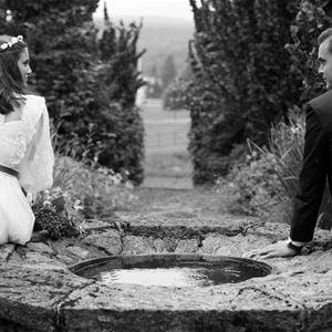 Black and white photo of a wedding couple sitting on each side of a fountain.