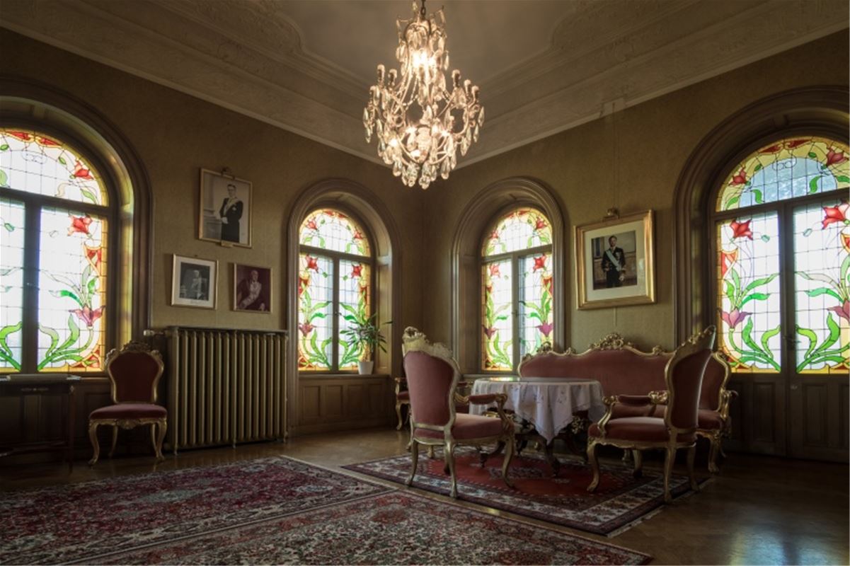 A large hall with a crystal chandelier, windows with floral paintings and Rococo-style furniture.