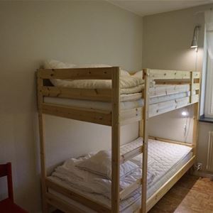 A bunkbed in pine placed beside a window with white curtains. 