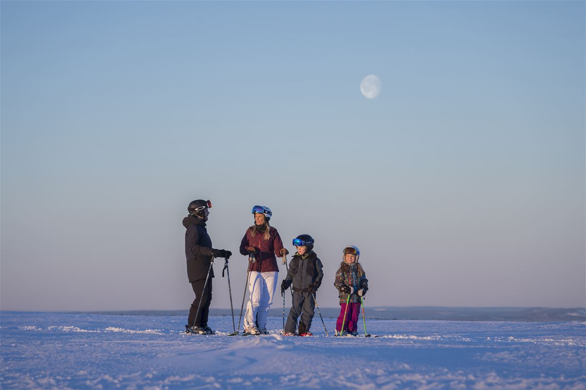 Familj som står med skidor och pratar uppe på fjället.