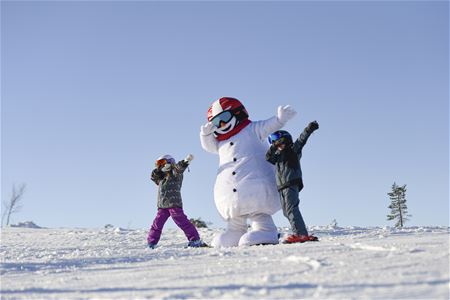 Två barn leker med en mänsklig stor snögubbe. 